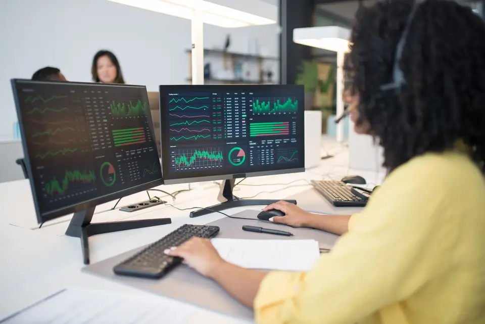 Analyst working at two monitors showing green data dashboards