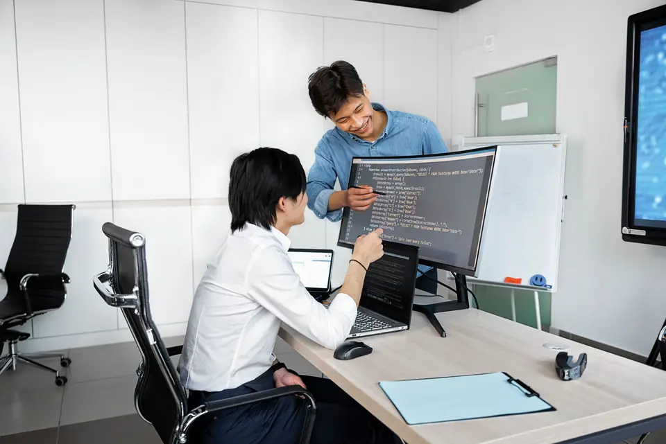 Two developers reviewing code on a curved monitor